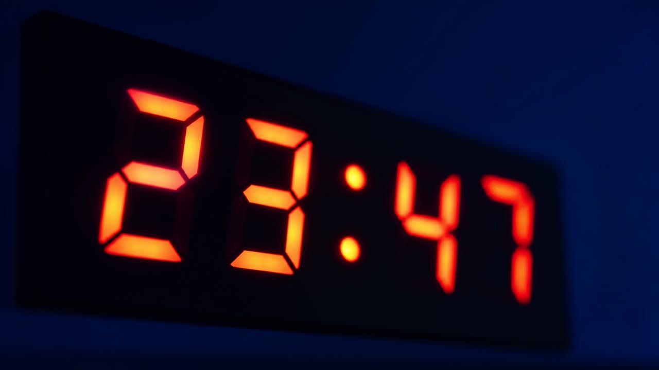 Glowing digital LED clock display in the dark, illustrating letting AI do the repetitive reps to free up time for human judgment.
